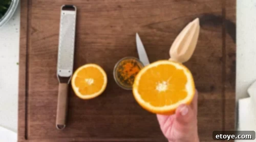 A close-up of a hand zesting a fresh orange over a bowl, with the freshly squeezed juice beside it, emphasizing the vibrant, aromatic, and fresh citrus elements integral to the walnut vinaigrette.
