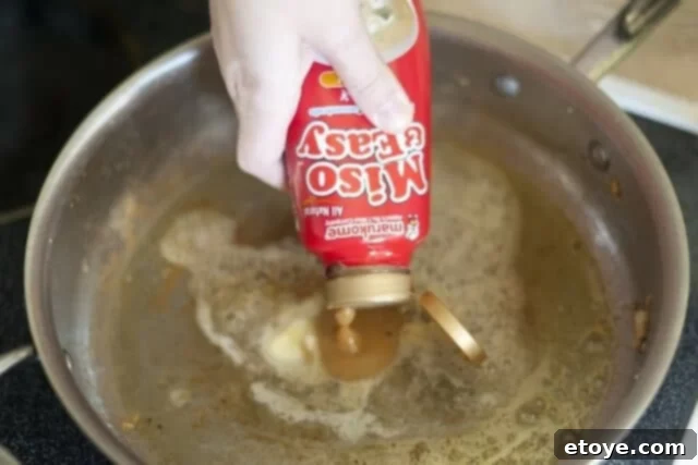 Rich Miso Chicken Pasta 7 Greek yogurt being stirred into the butter and miso mixture in the skillet, creating a creamy sauce base.