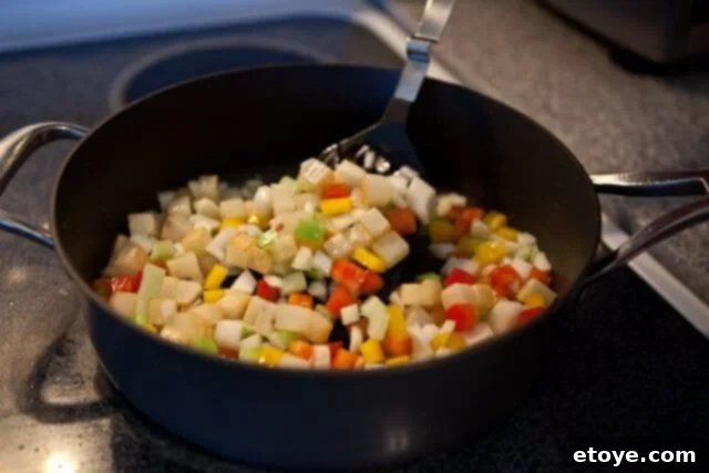 Sautéing diced vegetables including bell pepper, onion, celery, and garlic with browned potatoes in a pan