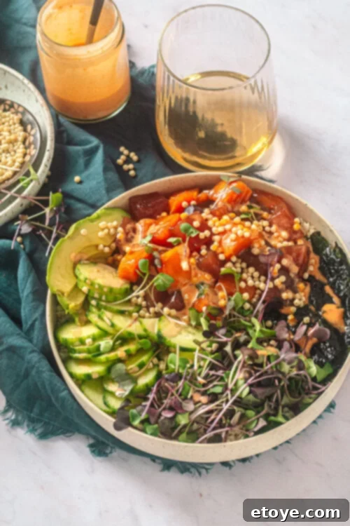 Irresistible Tuna and Salmon Sushi Bowl with Spicy Mayo 3 Close-up of a Tuna and Salmon Sushi Bowl with a generous drizzle of spicy mayo, accompanied by a wine glass and sauce dish.