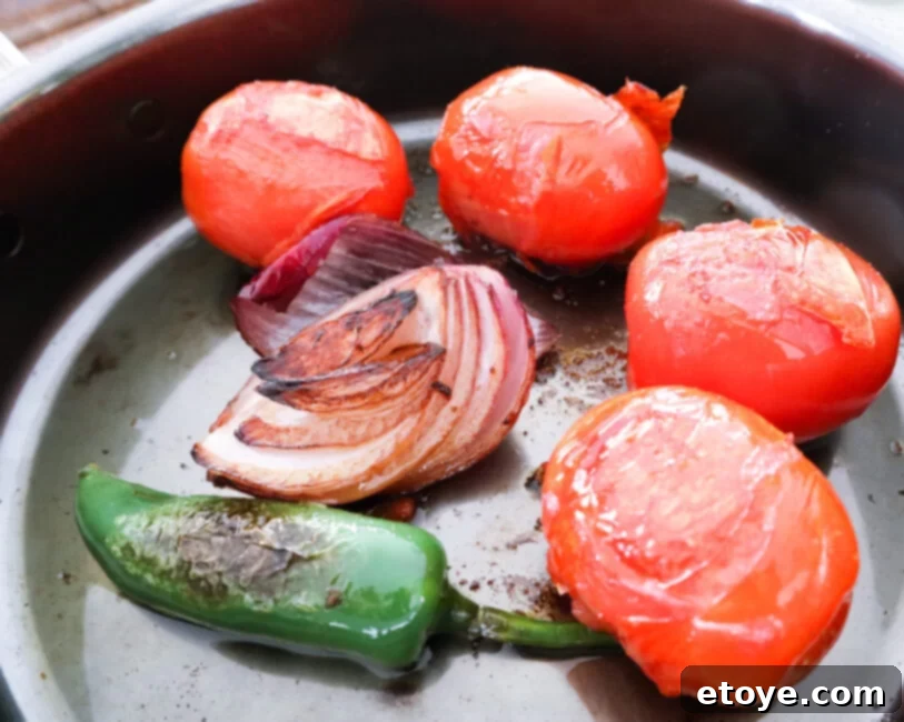 Fire-Kissed Tomato Salsa 2 Charred tomatoes, onions, and jalapenos in a pan, ready for blending into a vibrant salsa.