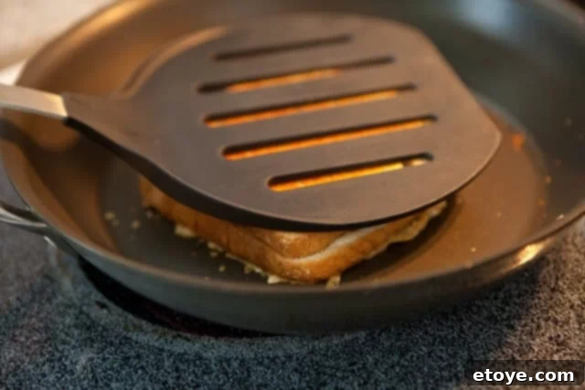 Frico-Crusted Grilled Cheese 6 A large spatula pressing down firmly on the grilled cheese sandwich to weld the crispy frico to its base.