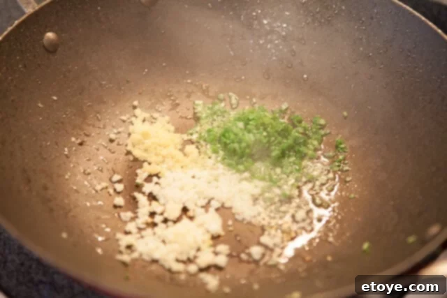 Sautéing Aromatics for Deep Flavor Chili and Onion Flash Fry for Sauce Base - Aromatics sizzling in a wok with rendered fat