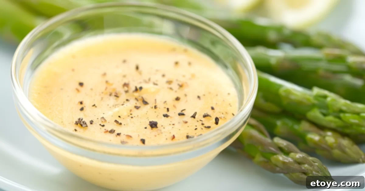 Hollandaise Sauce in a glass bowl with pepper and asparagus on the side