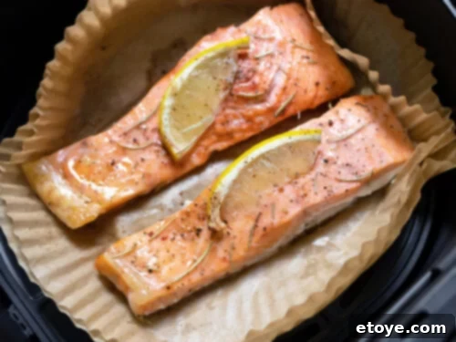 Crispy salmon fillets with lemon slices cooking on a custom-fit, perforated parchment liner in an air fryer, highlighting easy food removal.