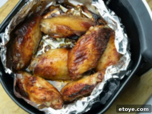 Close-up of crispy chicken pieces being cooked in an air fryer, with a small piece of aluminum foil folded to create a divider.