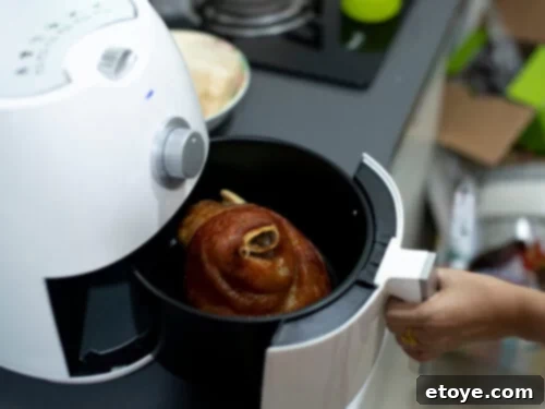 A perfectly cooked pork shoulder joint sits in an air fryer basket, showing the golden-brown crust achieved with this cooking method.