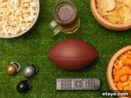 Football with various Super Bowl party essentials like snacks, beverages, and a remote control.