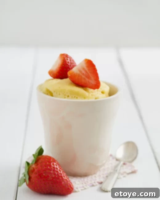 Effortless Microwave Cleaning 3 vanilla cake in a white mug topped with strawberries.