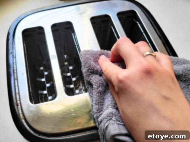 Get a Spotless Toaster Fast and Effortlessly 9 A hand wiping down the exterior of a toaster with a cleaning cloth