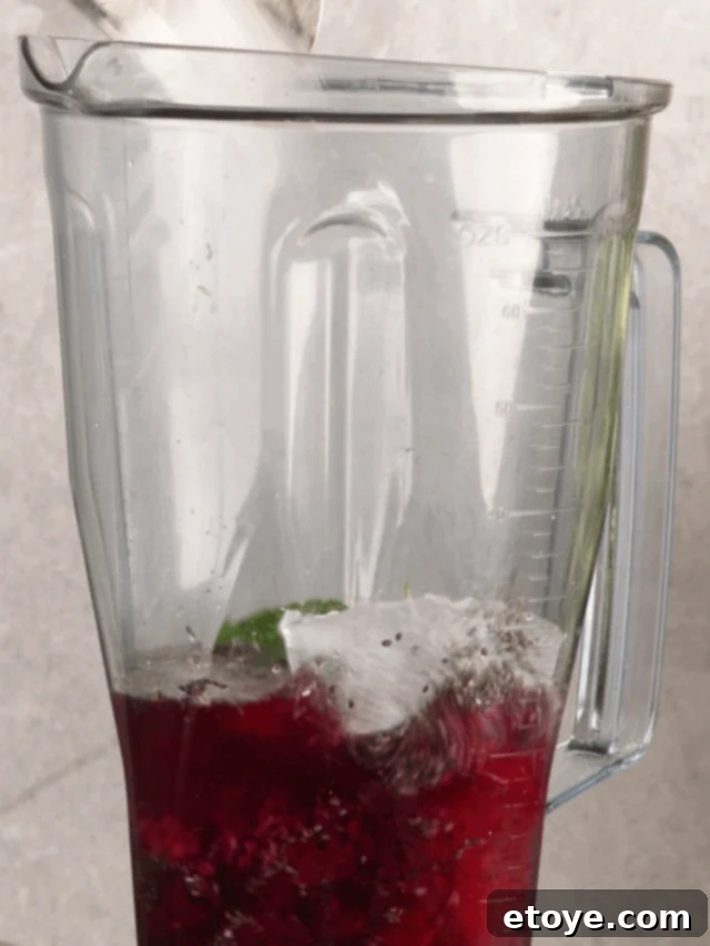 Dragon Fruit Hibiscus Coconut Refresher 4 Overhead shot of a glass of Dragon Fruit Chill Smoothie next to fresh dragon fruit slices, hibiscus flowers, and mint leaves, arranged on a light surface.
