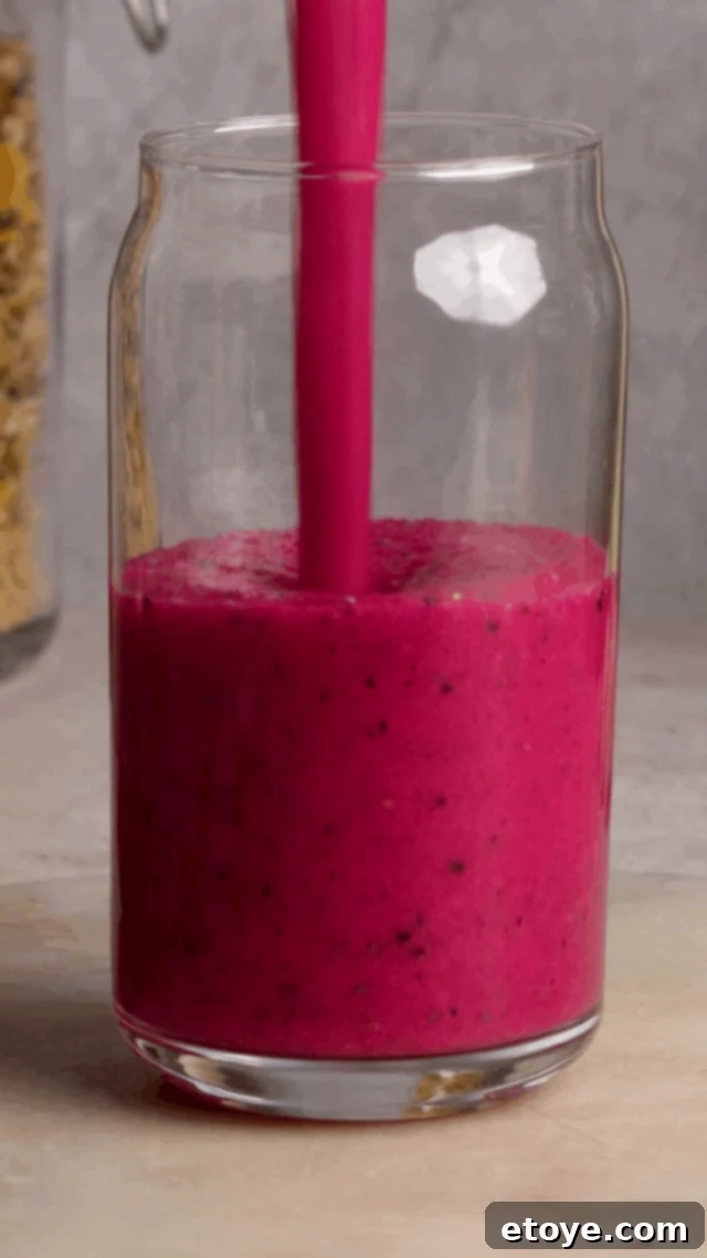 Dragon Fruit Hibiscus Coconut Refresher 6 A person holding a glass of Dragon Fruit Chill Smoothie, showcasing its beautiful pink color and refreshing appeal in a bright setting.