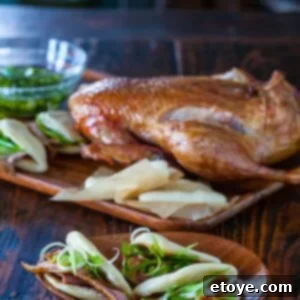 A beautifully roasted Chinese duck with golden-crispy skin, served alongside fluffy steamed buns.