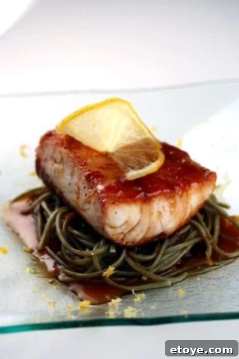 Delicious fish fillet with vibrant citrus soy sauce served alongside soba noodles, garnished with fresh herbs.