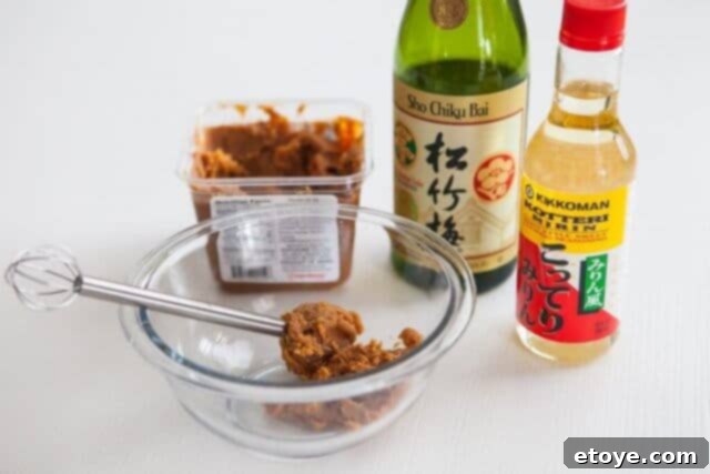Ingredients for miso salmon recipe, including miso paste, sake, and mirin, being whisked in a bowl.