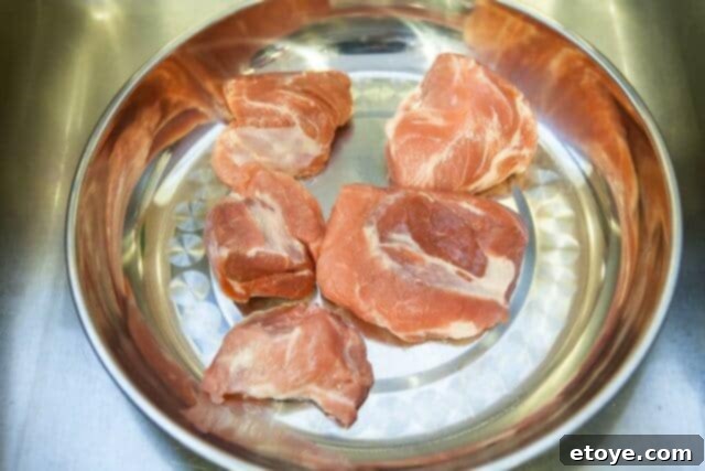 Raw pork pieces arranged in a shallow bowl, pre-cooking, ready for the par-boiling shortcut method.