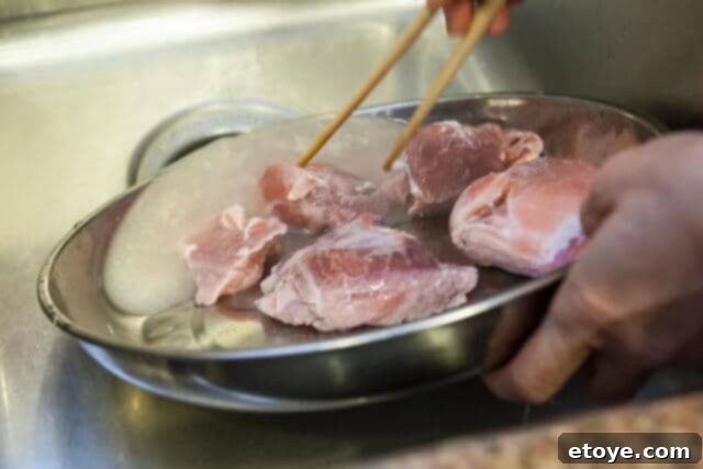 Par-boiled pork in a dish after draining the first cloudy water, showing clearer meat.