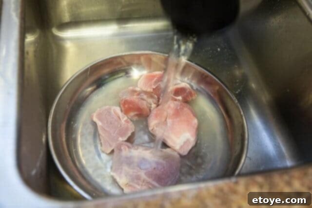 Fresh boiling water being poured over par-boiled pork in a dish for a second rinse.