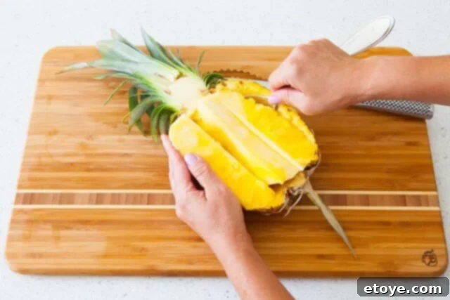 Scooping out the remaining pineapple flesh using a large spoon, being careful not to pierce the skin