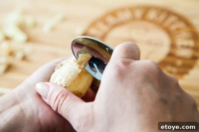 Making the Most of Leftover Ginger 5 A hand demonstrating how to easily peel ginger using the edge of a small spoon