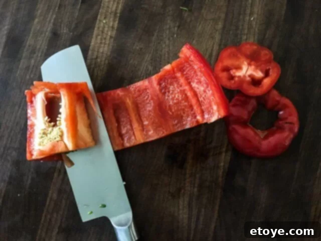 Close-up of a knife removing the core and ribs from a bell pepper, demonstrating proper prep technique.