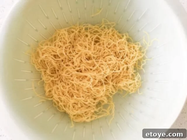 Drained Chinese noodles, lightly coated with sesame oil to prevent sticking, ready for stir-frying.