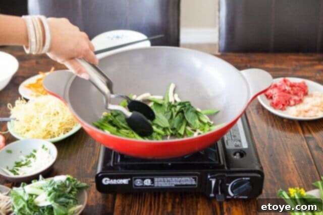 Assorted vegetables being added to the wok in sequence, longest-cooking first.