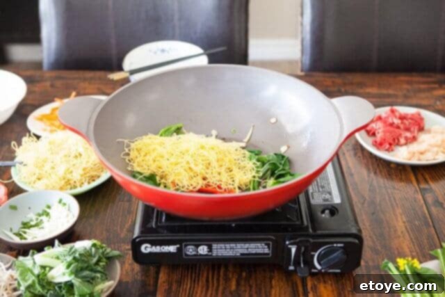 Noodles added to the wok with vegetables, ready to be mixed and heated.