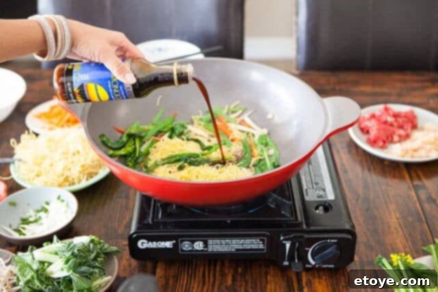 San-J Mongolian BBQ cooking sauce being poured into the wok with noodles and vegetables.
