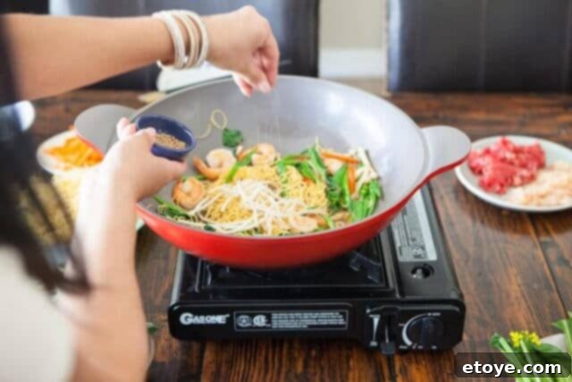 A close-up of roasted sesame seeds being sprinkled over the stir-fry in the wok.