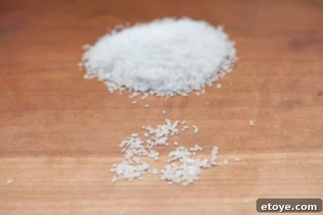 A bowl of Morton Kosher Salt next to a wooden cutting board with fresh vegetables, ready for seasoning