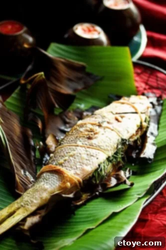 A beautifully grilled whole fish, seasoned with herbs and spices, elegantly presented on a banana leaf