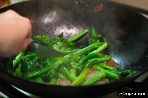 A knife piercing a stem of cooked Chinese Broccoli to test for tenderness