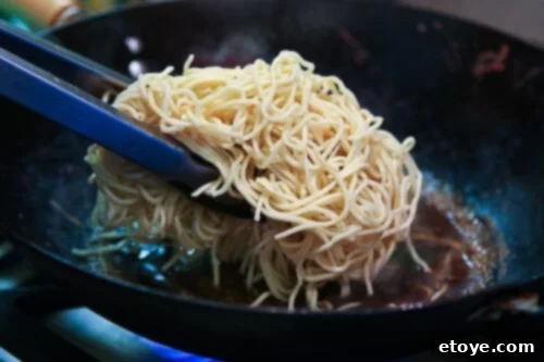 Cooked noodles being tossed in a wok with the stir-fry sauce, absorbing the flavors