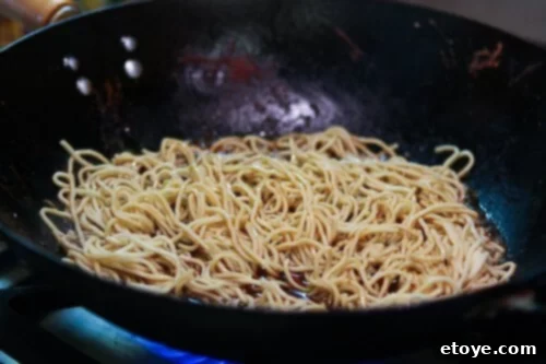 Close-up of noodles fully coated and absorbing the stir-fry sauce in the wok