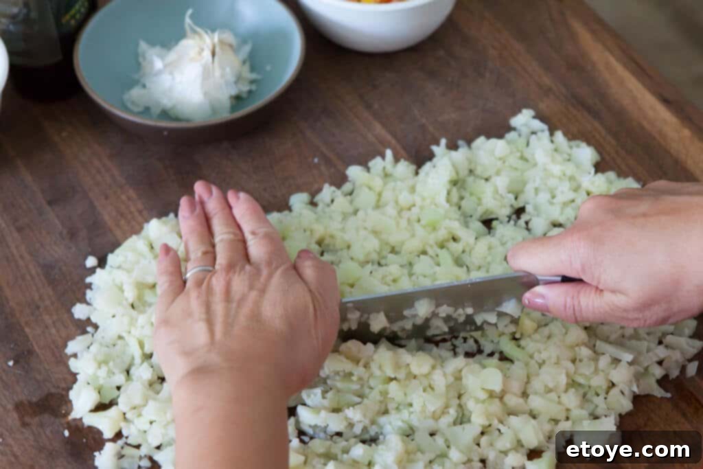 Close-up of cauliflower being finely minced with a chef's knife to create rice