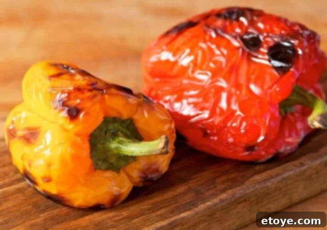 Multiple bell peppers roasting under a broiler on a baking sheet.