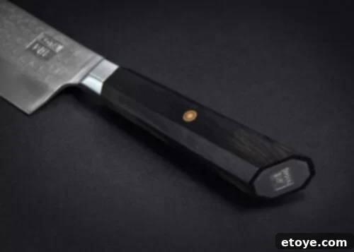 Detailed shot of the KOTAI Kiritsuke Chef Knife's ergonomic handle, highlighting the comfortable grip and stylish red accents against the black Pakkawood, designed for optimal user experience.