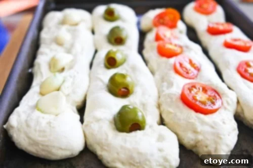 No-Knead Baguette loaves on a baking sheet, with whole garlic cloves, olives, and cherry tomatoes embedded