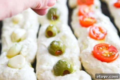 No-Knead Baguette loaves on a baking sheet, generously sprinkled with coarse salt after adding toppings