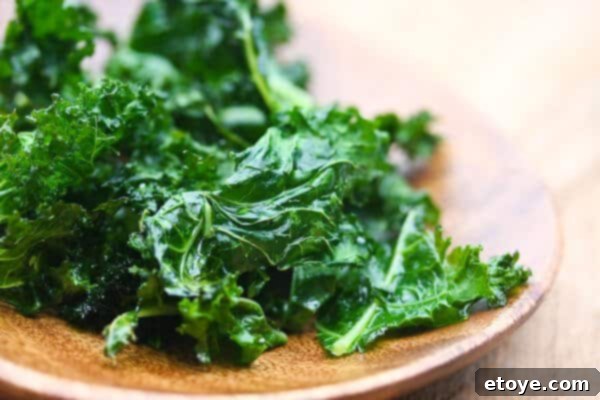 Perfectly baked crispy kale chips on a white plate, ready to be enjoyed