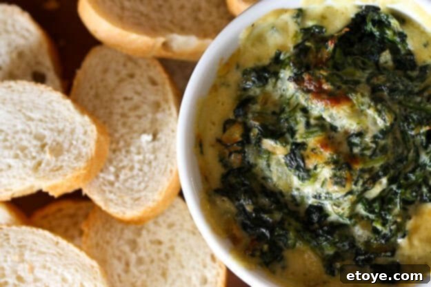 A freshly baked Warm Spinach Mascarpone Dip, still bubbling hot, presented in a small ramekin with various dipping options like crackers and bread slices