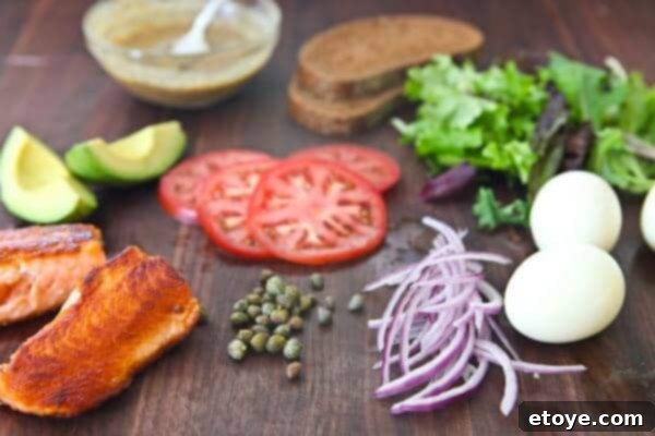 Open Face Salmon Sandwich Ingredients Fresh ingredients laid out for open face salmon sandwich: salmon fillets, egg, avocado, tomato, red onion, capers, greens, and rye bread.