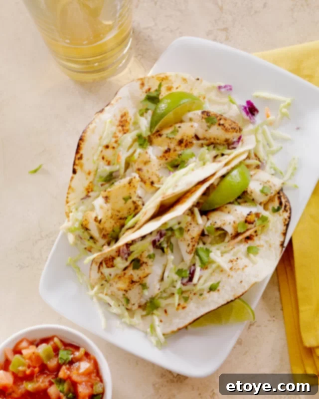 Fourth of July Feast Favorites 5 Two perfectly grilled fish tacos nestled in tortillas on a white plate, accompanied by a small bowl of fresh salsa.
