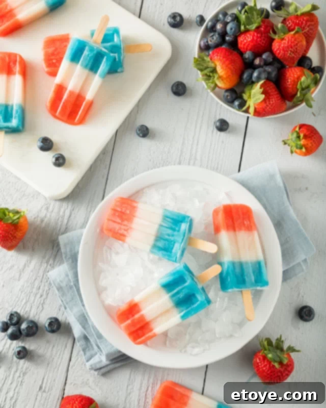 Fourth of July Feast Favorites 6 A festive display of red, white, and blue popsicles resting on a bed of ice, accompanied by a bowl of fresh strawberries and blueberries.